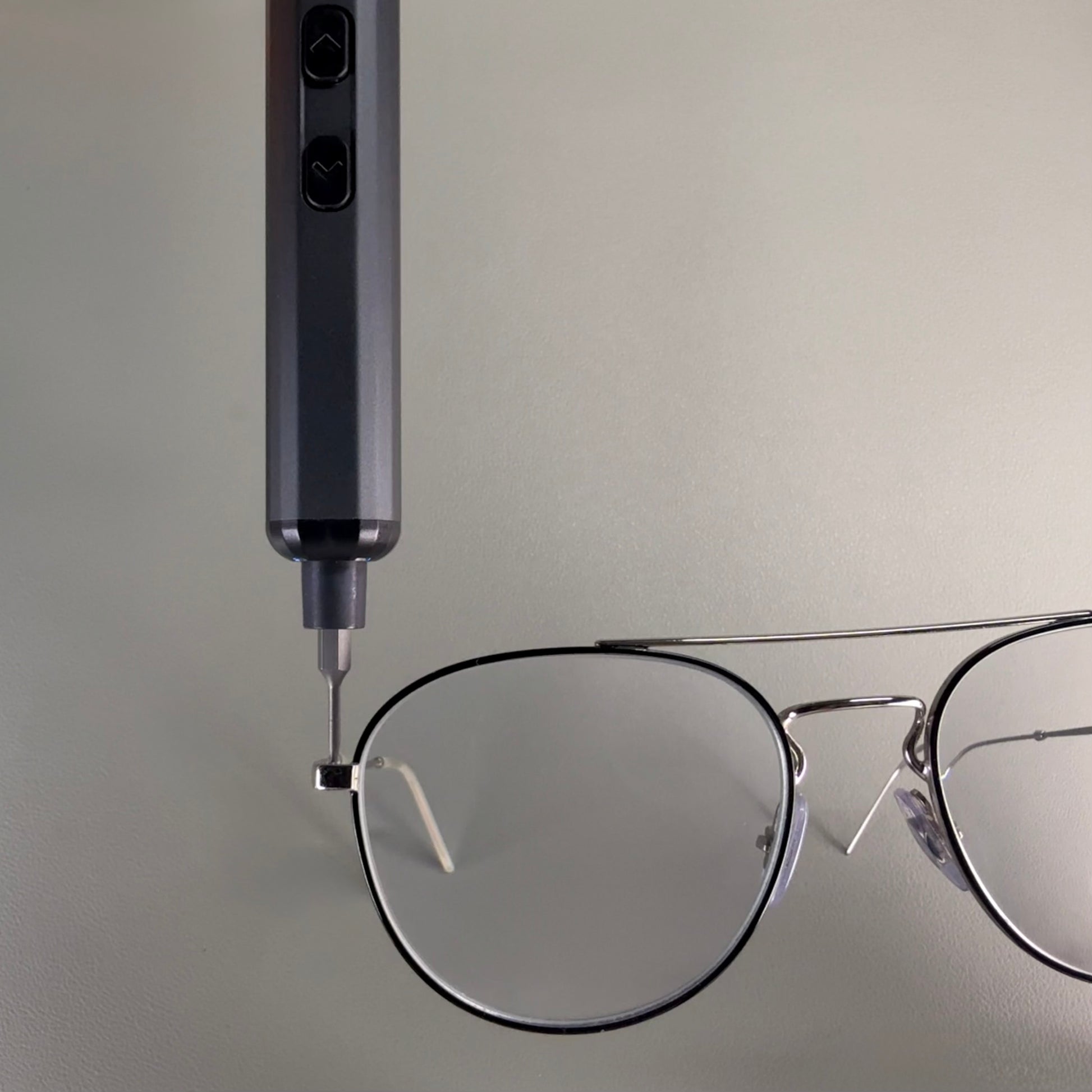 Close-up of an electric screwdriver tightening the hinge screw of a pair of metal-framed eyeglasses, emphasizing its use for micro precision repairs.