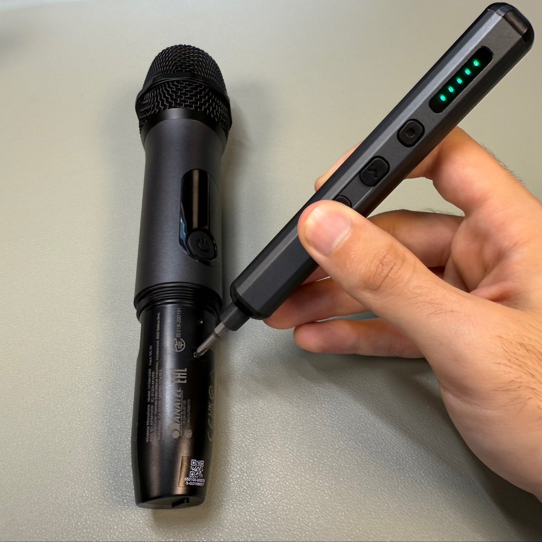 A sleek electric screwdriver being used to adjust the battery compartment of a wireless microphone, highlighting precision and control for audio equipment maintenance.